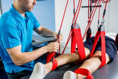 Fizyoterapi. Uzaklaştırma eğitim terapisi. Genç adam süspansiyon temelli egzersiz sistemiyle fitness çekiş terapisi yapıyor.