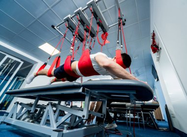 Fizyoterapi. Uzaklaştırma eğitim terapisi. Genç adam süspansiyon temelli egzersiz sistemiyle fitness çekme terapisi yapıyor. Omurgadaki ağrının tedavisi.