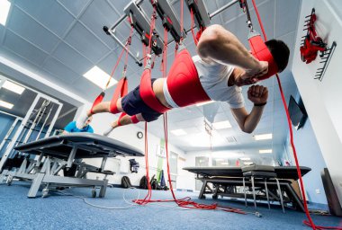 Fizyoterapi. Uzaklaştırma eğitim terapisi. Genç adam süspansiyon temelli egzersiz sistemiyle fitness çekme terapisi yapıyor. Omurgadaki ağrının tedavisi.