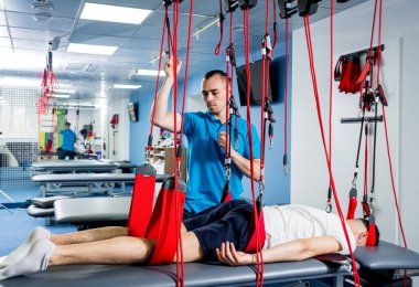 Fizyoterapi. Uzaklaştırma eğitim terapisi. Genç adam süspansiyon temelli egzersiz sistemiyle fitness çekiş terapisi yapıyor.