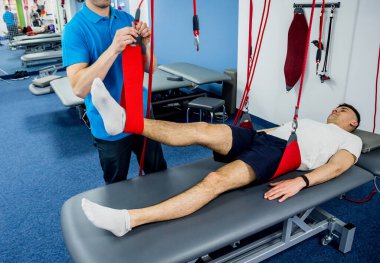 Fizyoterapi. Uzaklaştırma eğitim terapisi. Genç adam süspansiyon temelli egzersiz sistemiyle fitness çekme terapisi yapıyor. Omurgadaki ağrının tedavisi.