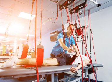 Fizyoterapi. Uzaklaştırma eğitim terapisi. Genç adam süspansiyon temelli egzersiz sistemiyle fitness çekiş terapisi yapıyor.