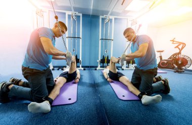 Rehabilitasyon terapisi. Fizyoterapistin gözetiminde paspas üzerinde egzersiz yapan genç bir adam. Omurgada tedavi ağrısı