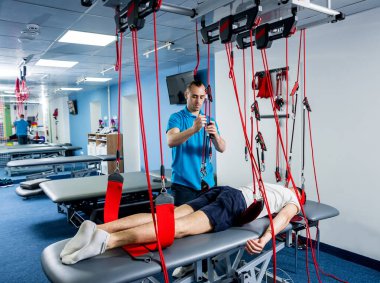 Fizyoterapi. Uzaklaştırma eğitim terapisi. Genç adam süspansiyon temelli egzersiz sistemiyle fitness çekiş terapisi yapıyor.