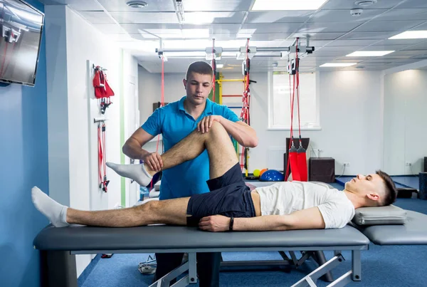 Rehabilitasyon terapisi. Rehabilitasyon merkezinde genç bir erkek hastayla çalışan fizyoterapist.