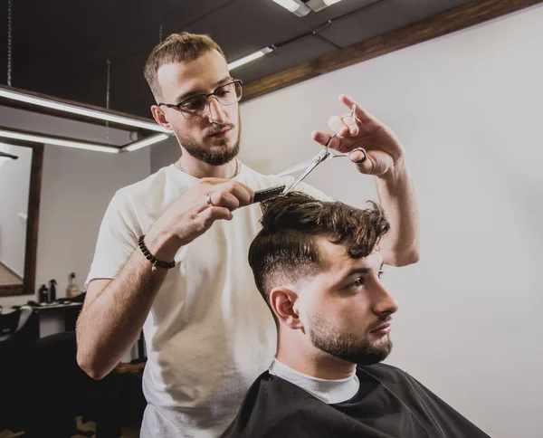 Young man with trendy haircut at barber shop. Barber does the hairstyle and beard trim. Concept barbershop.