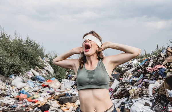 blindfolded female volunteer screams from powerlessness in dump of plastic rubbish