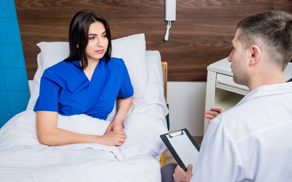 Traumatologist talking with young female patient in modern hospital