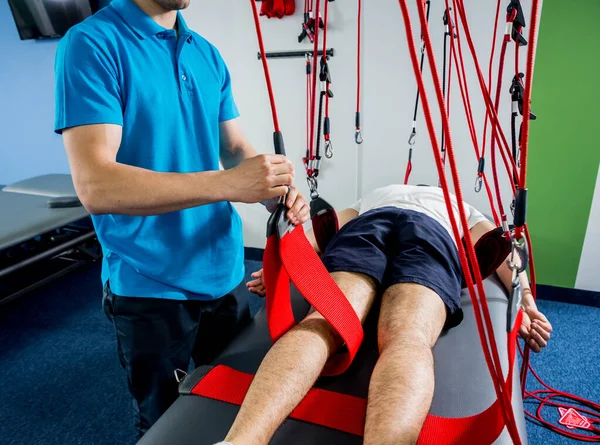 Fizyoterapi. Uzaklaştırma eğitim terapisi. Genç adam süspansiyon temelli egzersiz sistemiyle fitness çekme terapisi yapıyor. Omurgadaki ağrının tedavisi.