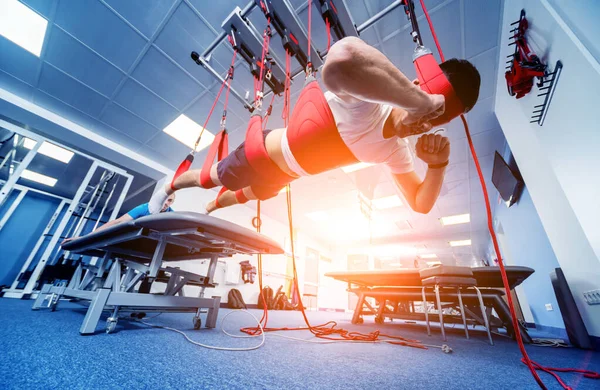 Physiotherapy. Suspension training therapy. Young man doing fitness traction therapy with suspension-based exercise training system. Treatment of pain in the spine.