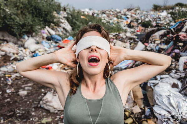 blindfolded female volunteer screams from powerlessness in dump of plastic rubbish