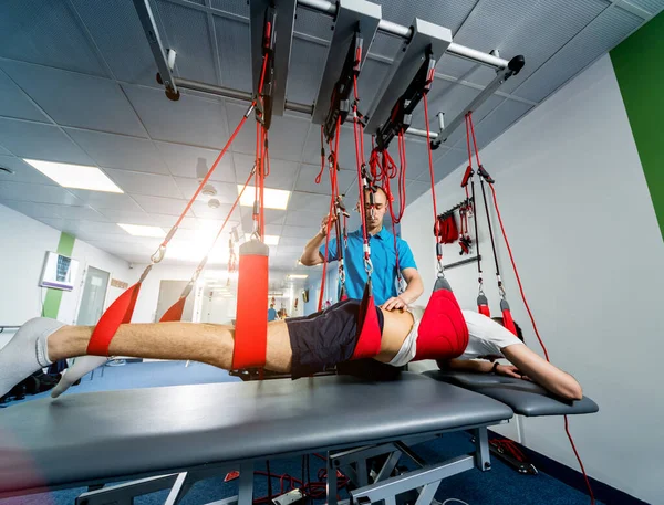 Physiotherapy. Suspension training therapy. Young man doing fitness traction therapy with suspension-based exercise training system.
