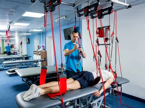 Fizyoterapi. Uzaklaştırma eğitim terapisi. Genç adam süspansiyon temelli egzersiz sistemiyle fitness çekiş terapisi yapıyor.