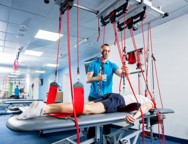 Fizyoterapi. Uzaklaştırma eğitim terapisi. Genç adam süspansiyon temelli egzersiz sistemiyle fitness çekiş terapisi yapıyor.