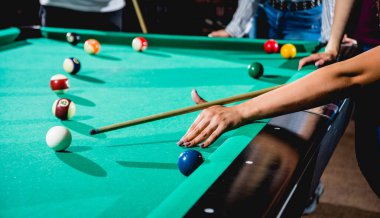 Genç bir kadın bilardoda topa vurmaya çalışıyor. Arka planda bilardo odası..