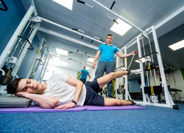 Rehabilitasyon terapisi. Fizyoterapistin gözetiminde paspas üzerinde egzersiz yapan genç bir adam. Omurgada tedavi ağrısı