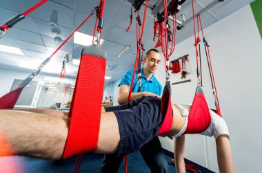 Fizyoterapi. Uzaklaştırma eğitim terapisi. Genç adam süspansiyon temelli egzersiz sistemiyle fitness çekiş terapisi yapıyor.