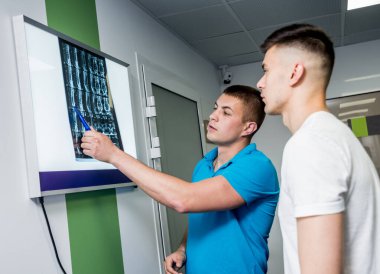 Genç bir erkek hasta olan fizyoterapist MRI filmini inceliyor. Rehabilitasyon Merkezi