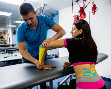 Kinesiotaping. Physical therapist applying tape to young beautiful womans spine, hand and cubit. Physiotherapy. clipart