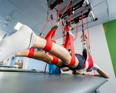 Fizyoterapi. Uzaklaştırma eğitim terapisi. Genç adam süspansiyon temelli egzersiz sistemiyle fitness çekme terapisi yapıyor. Omurgadaki ağrının tedavisi.