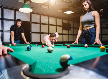 Genç adam bilardoda topa vurmaya çalışıyor. Havuz arkaplanı