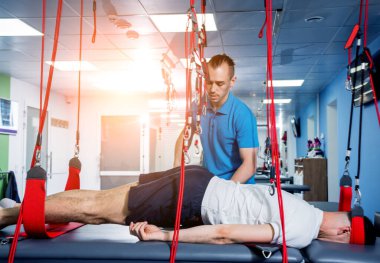 Fizyoterapi. Uzaklaştırma eğitim terapisi. Genç adam süspansiyon temelli egzersiz sistemiyle fitness çekiş terapisi yapıyor.