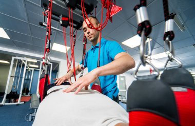 Uzaklaştırma eğitim terapisi. Genç adam süspansiyon temelli egzersiz sistemiyle fitness çekiş terapisi yapıyor.