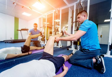 Rehabilitasyon terapisi. Fizyoterapistin gözetiminde paspas üzerinde egzersiz yapan genç bir adam. Omurgada tedavi ağrısı