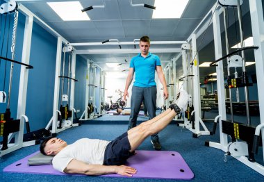 Rehabilitasyon terapisi. Fizyoterapistin gözetiminde paspas üzerinde egzersiz yapan genç bir adam. Omurgada tedavi ağrısı