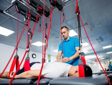 Fizyoterapi. Uzaklaştırma eğitim terapisi. Genç adam süspansiyon temelli egzersiz sistemiyle fitness çekiş terapisi yapıyor.