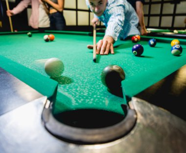 Genç adam bilardoda topa vurmaya çalışıyor. Havuz arkaplanı
