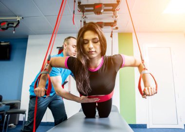 Genç bir kadın süspansiyon temelli egzersiz sistemiyle fitness çekiş terapisi yapıyor. Fizyoterapi kavramı