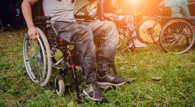 Kamp alanında arkadaşlarıyla dinlenen engelli bir adam. Çadırların arka planında, ormanda tekerlekli sandalye. Kamp yapmak. Yaz zamanı.