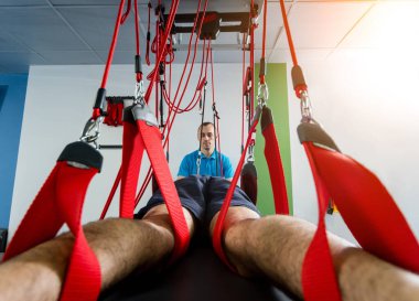 Fizyoterapi. Uzaklaştırma eğitim terapisi. Genç adam süspansiyon temelli egzersiz sistemiyle fitness çekiş terapisi yapıyor.