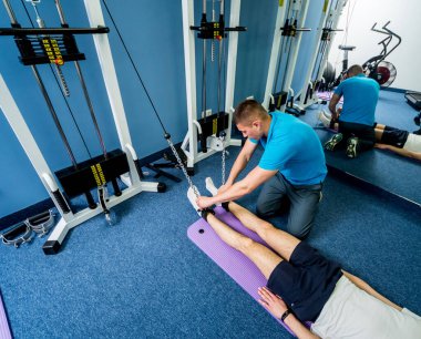 Rehabilitasyon terapisi. Fizyoterapistin gözetiminde paspas üzerinde egzersiz yapan genç bir adam. Omurgada tedavi ağrısı