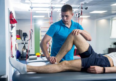 Rehabilitasyon terapisi. Rehabilitasyon merkezinde genç bir erkek hastayla çalışan fizyoterapist.