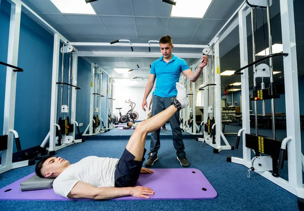 Rehabilitation therapy. Young man doing exercises on mat under supervision of physiotherapist. Treatment pain in spine