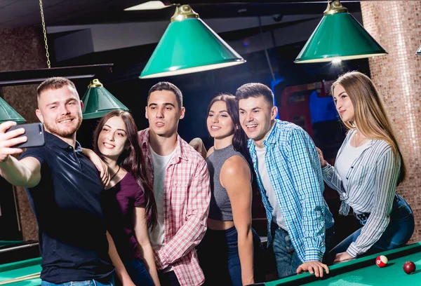 A group of friends makes a selfie at the pool table. Posing with a cue in their hands.