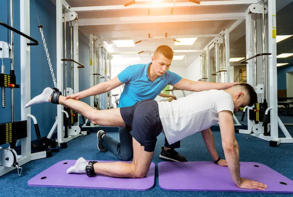 Rehabilitation therapy. Young man doing exercises on mat under supervision of physiotherapist. Treatment pain in spine