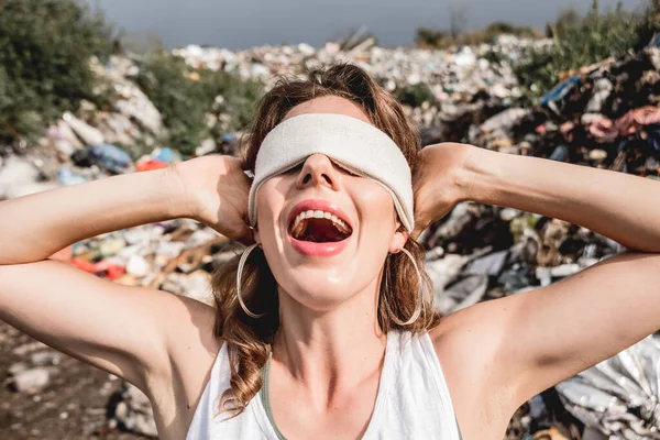 blindfolded female volunteer screams from powerlessness in dump of plastic rubbish