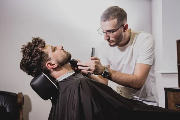 Young man with trendy haircut at barber shop. Barber does the hairstyle and beard trim. Concept barbershop.