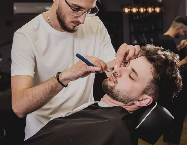 Young man with trendy haircut at barber shop. Barber does the hairstyle and beard trim. Concept barbershop.