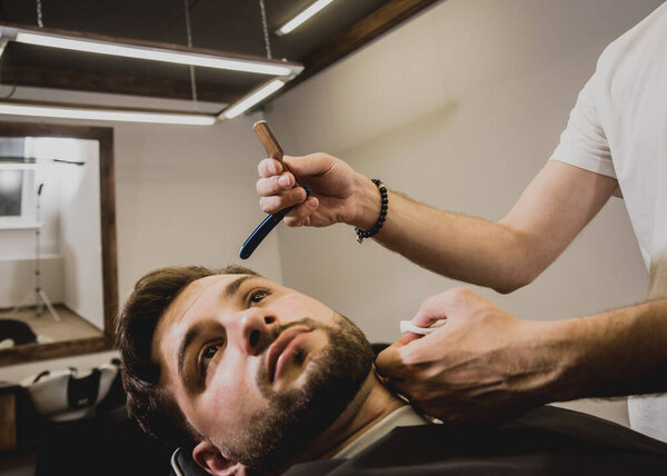 Young man with trendy haircut at barber shop. Barber does the hairstyle and beard trim. Concept barbershop.