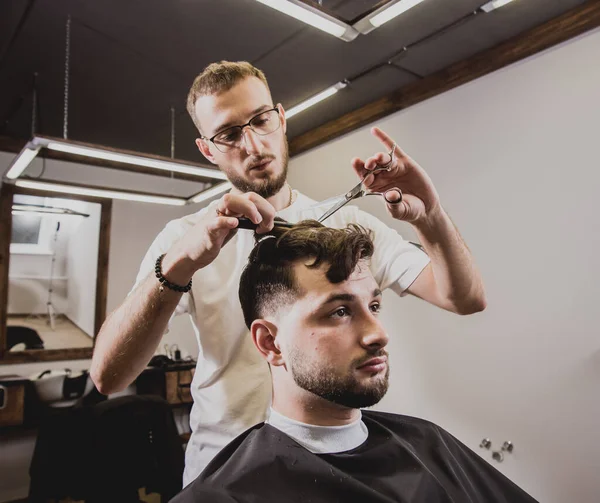 Young man with trendy haircut at barber shop. Barber does the hairstyle and beard trim. Concept barbershop.