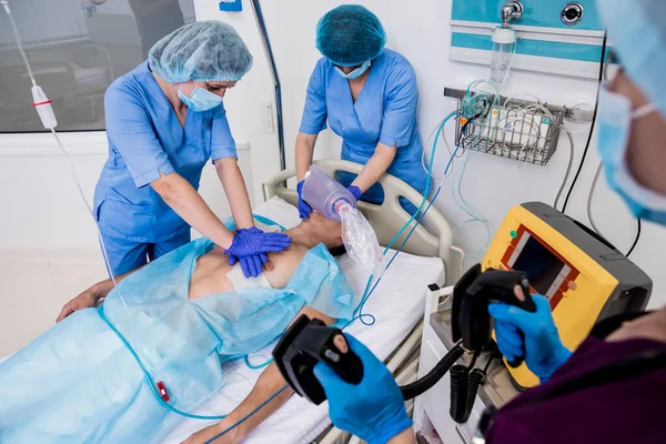 Los médicos dan reanimación a un paciente masculino en la sala de emergencias. Masaje cardíaco — Foto de Stock