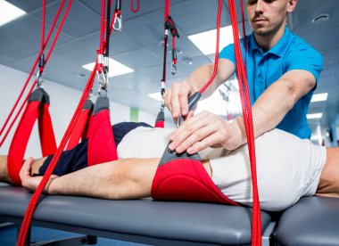 Fizyoterapi. Uzaklaştırma eğitim terapisi. Genç adam süspansiyon temelli egzersiz sistemiyle fitness çekiş terapisi yapıyor.