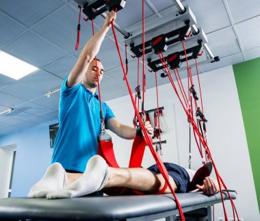 Fizyoterapi. Uzaklaştırma eğitim terapisi. Genç adam süspansiyon temelli egzersiz sistemiyle fitness çekiş terapisi yapıyor.