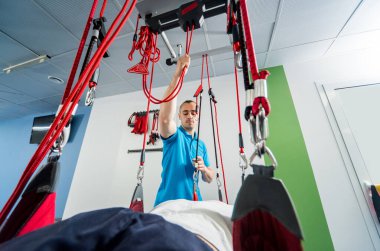 Fizyoterapi. Uzaklaştırma eğitim terapisi. Genç adam süspansiyon temelli egzersiz sistemiyle fitness çekiş terapisi yapıyor.