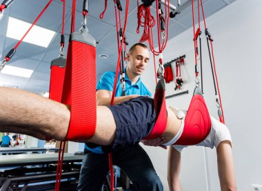 Fizyoterapi. Uzaklaştırma eğitim terapisi. Genç adam süspansiyon temelli egzersiz sistemiyle fitness çekiş terapisi yapıyor.