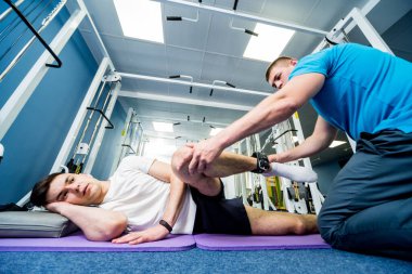 Rehabilitasyon terapisi. Fizyoterapistin gözetiminde paspas üzerinde egzersiz yapan genç bir adam. Omurgada tedavi ağrısı